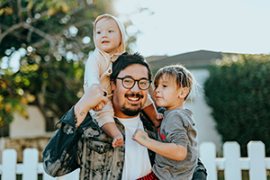 Father carrying one child on his shoulder and the other on his opposite arm