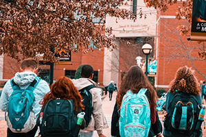 Backs of students in blue backpacks walking through college campus