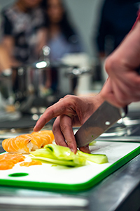 Close up of hand on knife slicing cucumbers on a cutting board