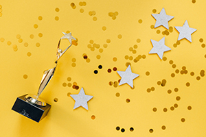 An award laying crossways with stars and gold confetti sprinkled against a yellow background