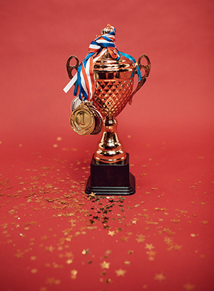 Trophy with a ribbon wrapped around it and gold confetti beneath it against a red background