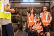 Man giving a tour of a brewery to three young individuals in orange vests