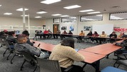 Group of people sitting around tables that are connected throughout a large room