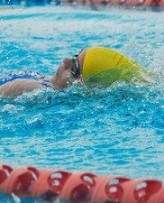 young person wearing a swimming cap and goggles swimming on their back in a pool