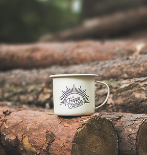 Close up of a mug that says "Happy Camper" on a log in the woods