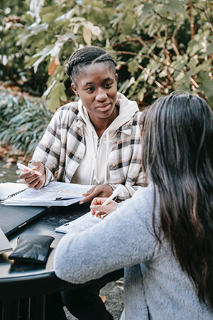 Two women speaking at a table with notebooks in front of them