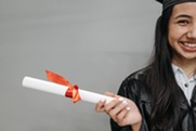 Young woman in a graduation cap and gown holding a rolled diploma