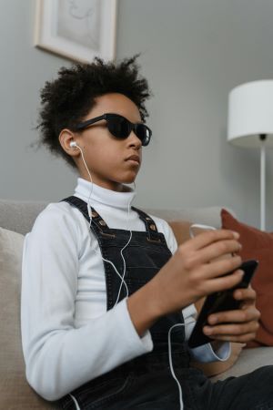 Teen boy in glasses holding a cell phone with headphones attached to it