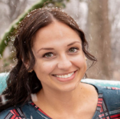 Sam Duke smiling while outside with snow flurries in her hair and a tree in the background