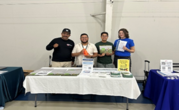 Agricultural Employment Liaisons holding up flyers while standing behind a table