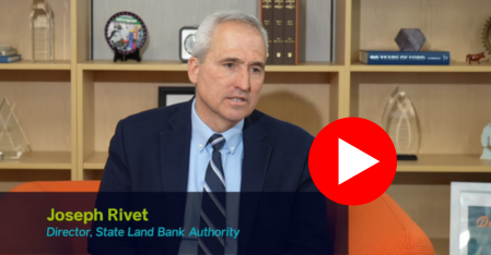 youtube thumbnail with play button, still shot of joseph rivet director of state land bank authority sitting in office