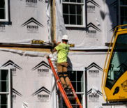 construction worker on latter working on home next to construction machine