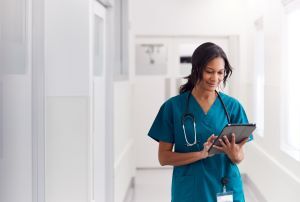 Woman in scrubs walking through hospital while holding clipboard