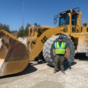 Nathan in construction gear standing in front of construction vehicles