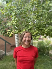 Aly Pindar wearing a red shirt and standing outside with trees in the background