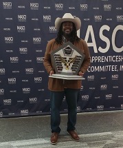 Anwar, a Black man in a cowboy hat, holding a MASCI award
