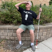 Man holding a walking stick sitting down and shielding his eyes