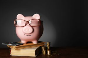 Piggy bank with glasses on top of coins and books on a table