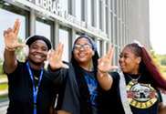 Three GVSU students making a sign with their right hands