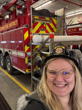 Abigail Frost wearing a fire hat and standing in front of a fire truck