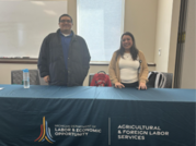 AFLS staff standing behind a table with an AFLS cover during job fair
