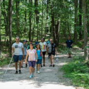 Group of students and adults using walking sticks walking through a trail