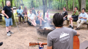 Group of young adults sitting around a camp fire during the day