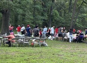 Large group of people around a picnic table outside