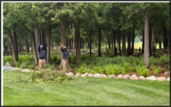 Two people wearing blue shirts waving while standing underneath the trees