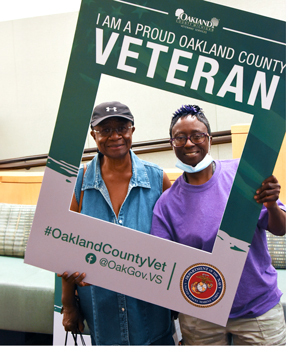 Two people holding a selfie frame reading "I am a proud Oakland County Veteran"