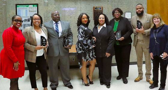 Eight people stand together in the lobby of the Oakland County Board of Commissioners Auditorium, five of them hold Black Excellence Awards