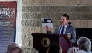 Commissioner Miller holds up immigration papers of his grandfather while speaking at a podium