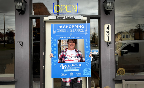 Woman holding a sign reading Shop Small standing in front of a store in Ortonville