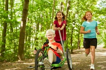 A child experiencing blindness riding a tricycle with friends outdoors.