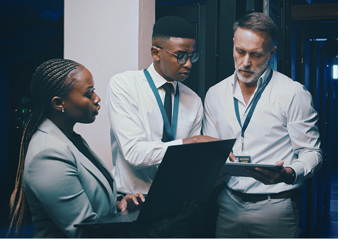 Three tech professionals looking at a laptop in a server room