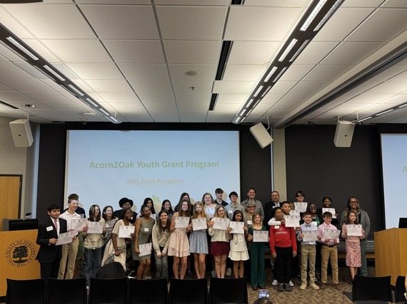 Group of students hold certificates in front of a sign that says Acorn2Oak 