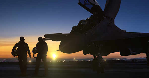 Two pilots walking away from a military jet at dusk.