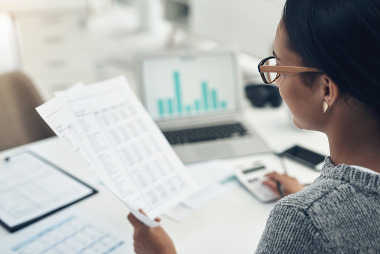Woman reviewing data on paper with computer showing bar graph