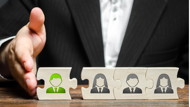 Person adding a puzzle piece to a puzzle - each puzzle piece has a face on it