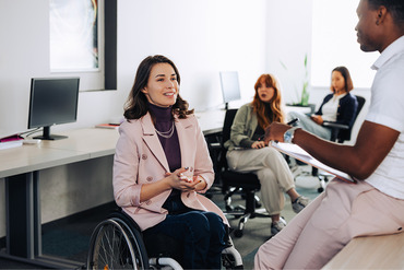 Woman in wheelchair speaking with others in office setting