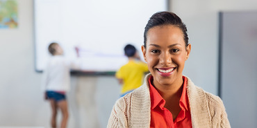 Woman smiling in school classroom students in background at the dry erase board