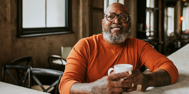 Man of color with glasses and drink cup at counter top.