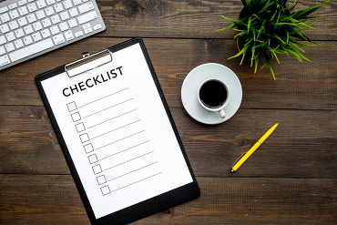 Clipboard with blank checklist on table with coffee cup, pen plant, and computer keyboard
