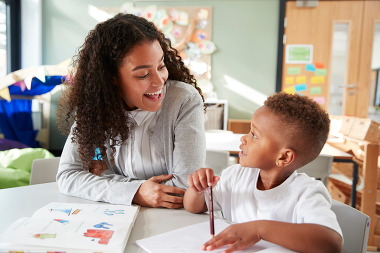 A teenage worker helps a young student with a written assignment in a classroom.