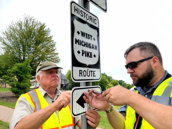 Local historian Blaine Knoll (left) and Ottawa County Land Use Specialist Andrew Roszkowski install a new West Michigan Pike sign.