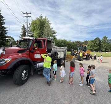 Road Commission employees escort children into a snow plow truck for a touch-a-truck event 