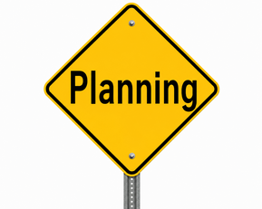 A yellow diamond-shaped road warning sign on a metal post with the word "Planning"