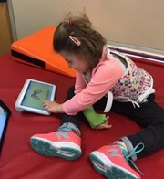 Young child in a pink shirt with a chest and arm brace using a communication device