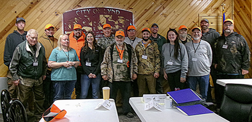 group shot of 16 accessible hunt participants and staff inside a lodge