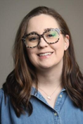 Headshot of a woman with shoulder length brown hair and spotted glasses smiling